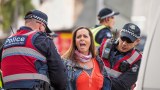 Police in vests hold down the arms of a woman in the Melbourne CBD.