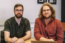 Two young men, both in glasses, sitting at a desk 