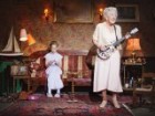 Older woman playing guitar as young girl sits on couch knitting