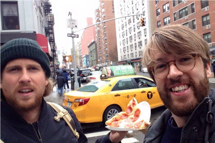 Two men on a NYC street holding a slice of pizza 