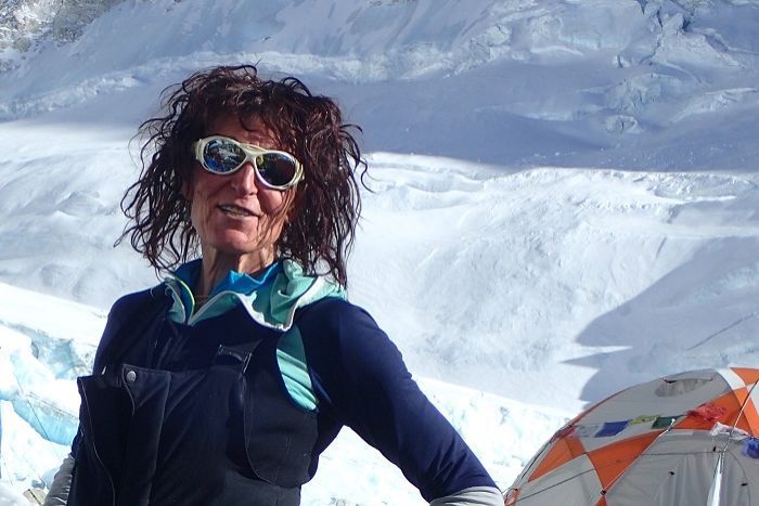 woman in ski goggle and ski suit stands in the snow with a tent in the background.