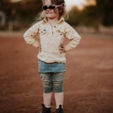 A young child wears sunglasses upside down, while giving a cheeky smile. 