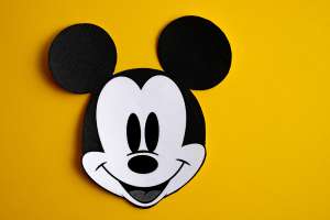 Black and white face of Mickey Mouse out of paper on a yellow background. Credit: ilikeyellow / Shutterstock