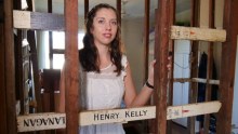 A woman in her 30s stands in her partly demolished bathroom with exposed crosses. 