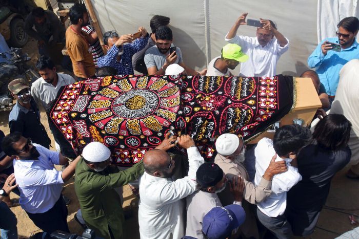 A group of men carrying a casket draped with a colourful red, yellow and black cloth, while others record the event with phones