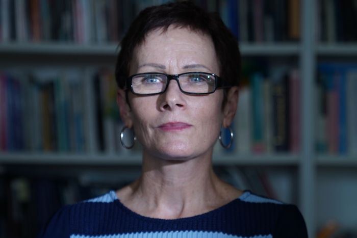 A woman looks away from the camera as she poses for a picture in front of a packed bookcase