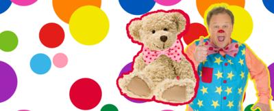 Tumble Ted is sat next to Mr Tumble who is smiling and giving a thumbs up to camera, on a spotted background.