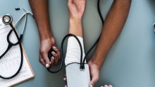 tightly cropped image, you can see a doctors hands giving a blood pressure test to someone with painted nails. 