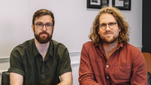 Two young men, both in glasses, sitting at a desk 