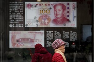 FILE - In a Monday, Feb. 18, 2019 file photo, women walk by a bank window panel displaying the security markers on the latest 100 Yuan notes in Beijing.