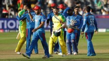 A batsman walks off after a Cricket World Cup match, as the opposing team stand on the pitch.