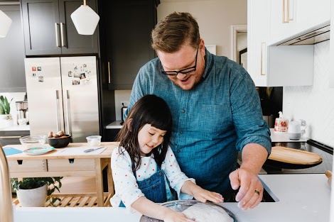 A happy father and his smiling daughter knead pizza dough onto a sheet in a kitchen as a way to help find a balance with technology.