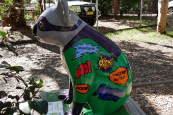 A bright sculpture of a koala, painted with colourful slogans saying habitat loss, ouch, help