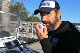 A man in a cap is on a boat, speaking into a radio mic