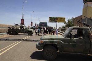 Demonstrators walk past army vehicles protecting the entrance to a rally near the military headquarters in Khartoum, Sudan, Monday, April 15, 2019.