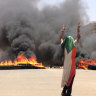 A protester wearing a Sudanese flag flashes the victory sign in front of burning tires and debris on road 60, near Khartoum's army headquarters during the violence on Monday.