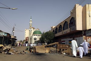 Sudanese men and a child headed to a mosque navigate a roadblock set by protesters on a main street in the Sudanese capital Khartoum to stop military vehicles from driving through the area on Wednesday, June 5, 2019