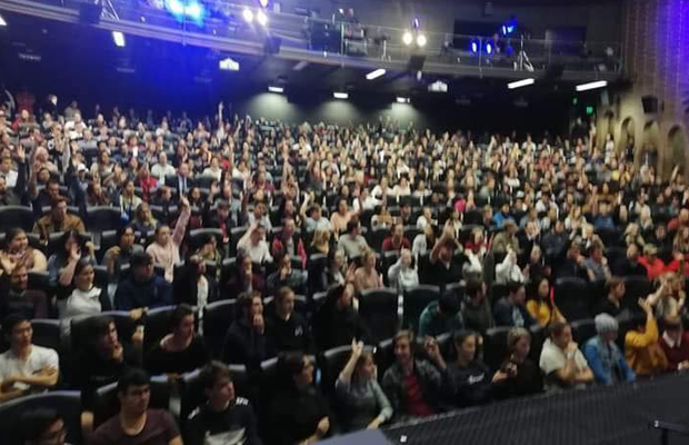 A photo of 500 students gathered in an auditorium all raising their hands