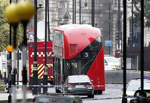 A forensics officers works near the scene near a car that crashed into security barriers outside the Houses of Parliament to the right of a bus in London, Tuesday, Aug. 14, 2018.