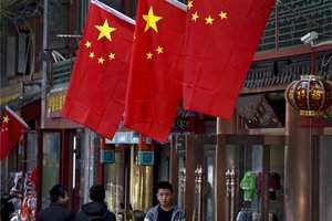 People walk by a worker waiting for customers outside his retail shop displaying national flags in the Chinese capital where the 19th Party Congress is held in Beijing, Sunday, Oct. 22, 2017.