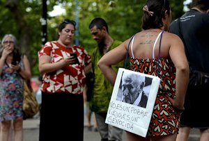 A woman stands with a picture of former police officer Miguel Etchecolatz that reads in Spanish, "He is not a poor man, he is a genocide" during a protest in Mar del Plata, Argentina, Friday, Dec. 29, 2017.