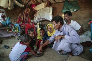 In this Oct. 1, 2018, file photo, a man feeds children halas, a climbing vine of green leaves, in Aslam, Hajjah, Yemen. The U.N. food agency has begun a partial suspension of food aid to areas of Yemen controlled by the rebels amid accusations they were diverting aid from the war-torn country's hungriest people, the group said Thursday, June 20, 2019.