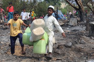 Young boys carry plastic containers to collect drinking water after a fire at a slum on the outskirts of Jammu, India, June 3, 2019.