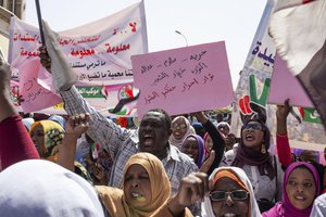 Protesters carry posters in Arabic that say, "Freedom, justice, and peace, and the revolution is the choice of the people," at the sit-in outside the military headquarters, in Khartoum, Sudan, Thursday, May 2, 2019