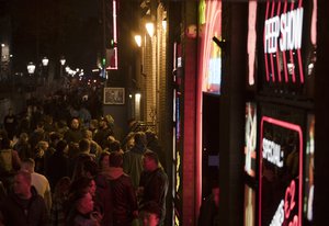 In this Friday March 29, 2019 file photo, tourists are bathed in a red glow emanating from the windows and peep shows' neon lights, packed shoulder to shoulder as they shuffle through the narrow alleys in Amsterdam's red light district, Netherlands.