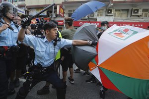 A police officer attacks protesters holding up umbrellas in Hong Kong Saturday, July 13, 2019