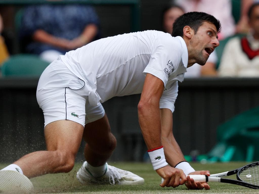 TOPSHOT - Serbia's Novak Djokovic slips on the grass as he plays Switzerland's Roger Federer during their men's singles final on day thirteen of the 2019 Wimbledon Championships at The All England Lawn Tennis Club in Wimbledon, southwest London, on July 14, 2019. (Photo by Adrian DENNIS / POOL / AFP) / RESTRICTED TO EDITORIAL USE