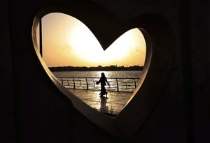 In this Sunday, May 11, 2014 file photo, a Saudi woman seen through a heart-shaped statue walks along an inlet of the Red Sea in Jiddah, Saudi Arabia.