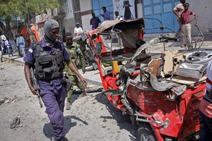 A policeman walks past a destroyed vehicle after an attack using an explosives-laden vehicle on a restaurant in Mogadishu, Somalia Thursday, March 28, 2019.