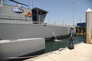 Cmdr. Bill Anderson, the military liaison to Defense Advanced Research Projects Agency (DARPA) coordinates with contractors from DARPA and Leidos as they run system checks on the Anti-Submarine Warfare Continuous Trail Unmanned Vessel (ACTUV) at Tenth Avenue Marine Terminal during a media availability