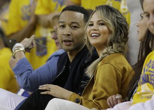 Musician John Legend, left, and his wife Chrissy Teigen watch during the first half of Game 1 of basketball's NBA Finals between the Golden State Warriors and the Cleveland Cavaliers in Oakland, Calif., Thursday, June 2, 2016