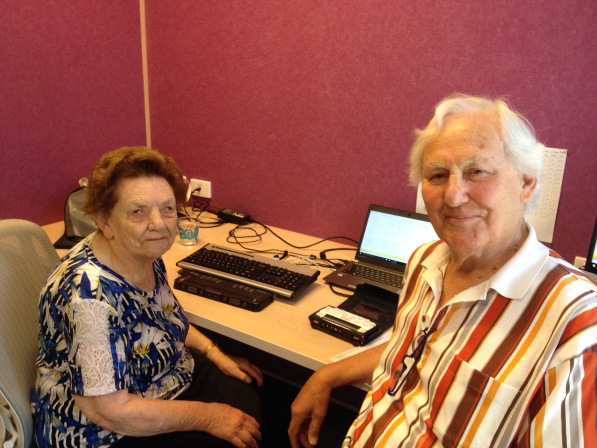 Dorothy and longtime volunteer John sit at a desk with braille equipment