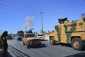 File - Smoke rises in the background from bombardment around the area as fighters with the Free Syrian army drive their pick-up truck, left, past a Turkey Armed Forces convoy, at a highway between Maaret al-Numan and Khan Sheikhoun in Idlib province, Syria, Monday, Aug. 19, 2019.