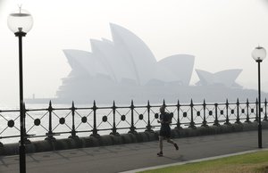 A jogger runs in the morning as smoke haze hangs over the Sydney Opera House in Sydney, Thursday, Nov. 21, 2019.