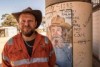 A man standing in front of an old water tank in outback Australia.