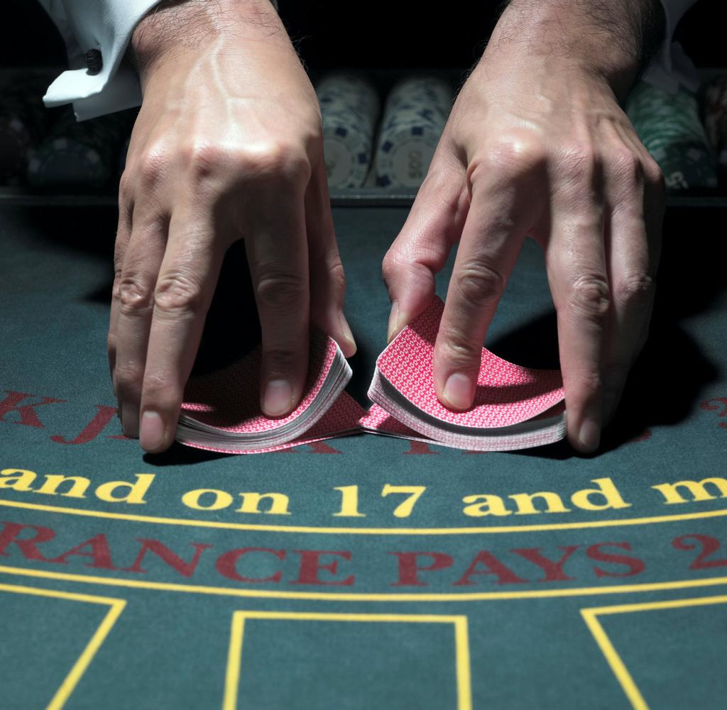 Male croupier shuffling cards at table, merging two piles, close-up