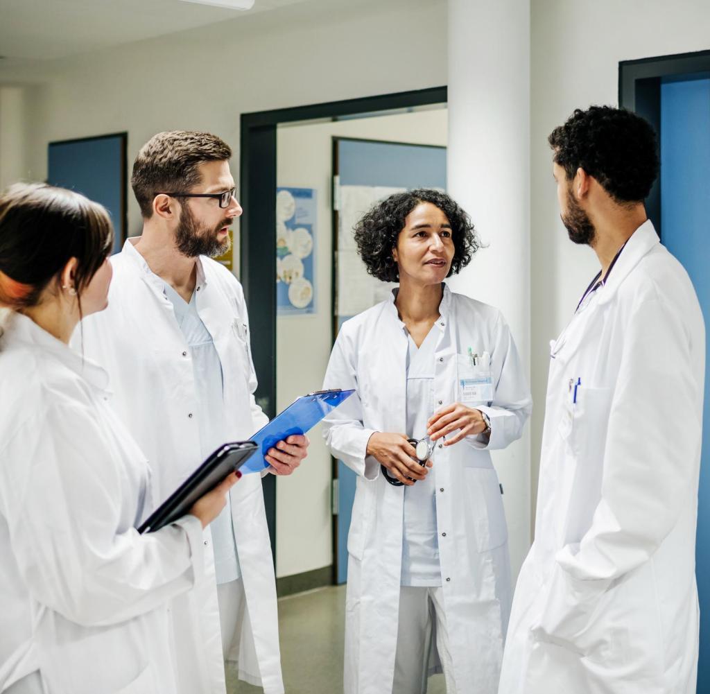 A group of clinical doctors with charts chatting on the ward at the hospital.