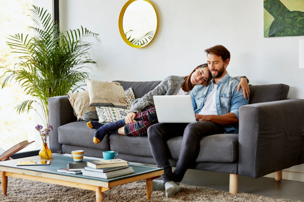 A woman and a man sitting on a couch looking at a laptop
