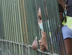 A girl wearing a mask to protect herself against the spread of the new coronavirus looks from her home in the neighborhood of Cristo del Consuelo as her family waits for food handouts from the local government of Guayaquil, Ecuador, Tuesday, April 14, 2020.