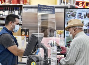 A grocery worker, wearing a protective mask and gloves, helps checking out a customer from behind a plexiglass barrier at the 99 Ranch Market in the Van Nuys section of Los Angeles on Tuesday May, 5, 2020.