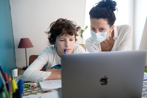 A pupil is working on Apple laptop with his mother at home during Coronavirus (Covid 19) outbreak, France