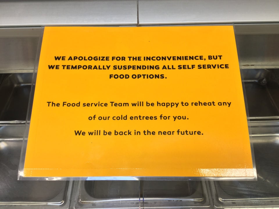 Orange printed sign apologizing for the temporary suspension of self service food options at Haight Street Market, place on top of the sneeze shield over an empty salad bar.