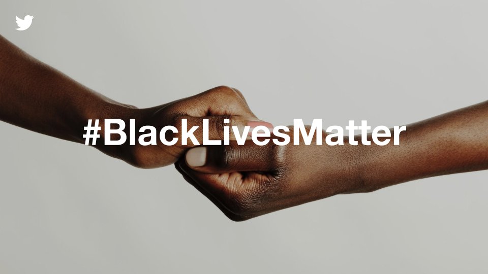 Two Black (African-American) hands holding on to each other with a tan background. The overlayed text is #BlackLivesMatter in white.