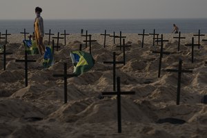 A woman walks amid symbolic graves on Copacabana beach, dug by activists from NGO Rio de Paz protesting the government's handling of the COVID-19 pandemic in Rio de Janeiro, Brazil, Thursday, June 11, 2020.