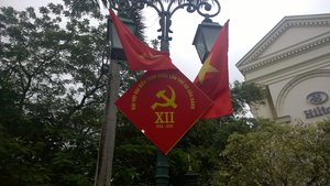 A street sign flanked by flags featuring meeting of the politburo of the Communist Party, Vietnam