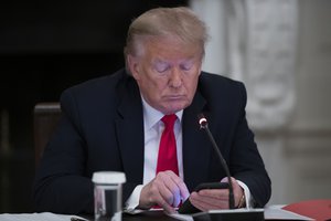 President Donald Trump looks at his phone during a roundtable with governors on the reopening of America's small businesses, in the State Dining Room of the White House, Thursday, June 18, 2020, in Washington